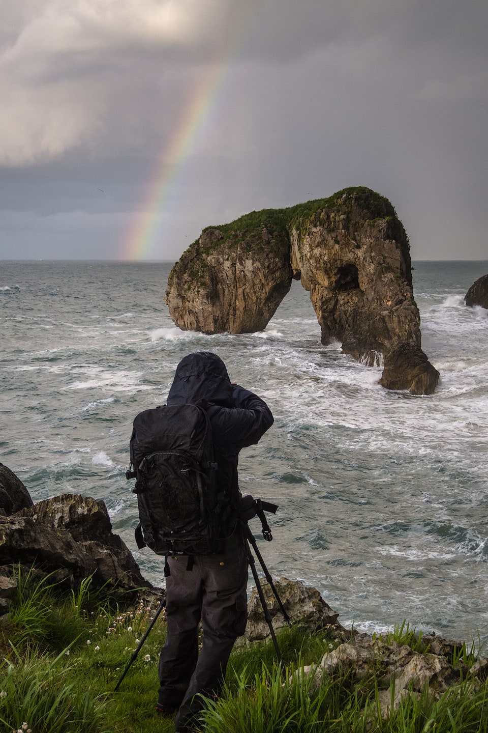 Photographer with tripod shooting a rainbow on the coast.
