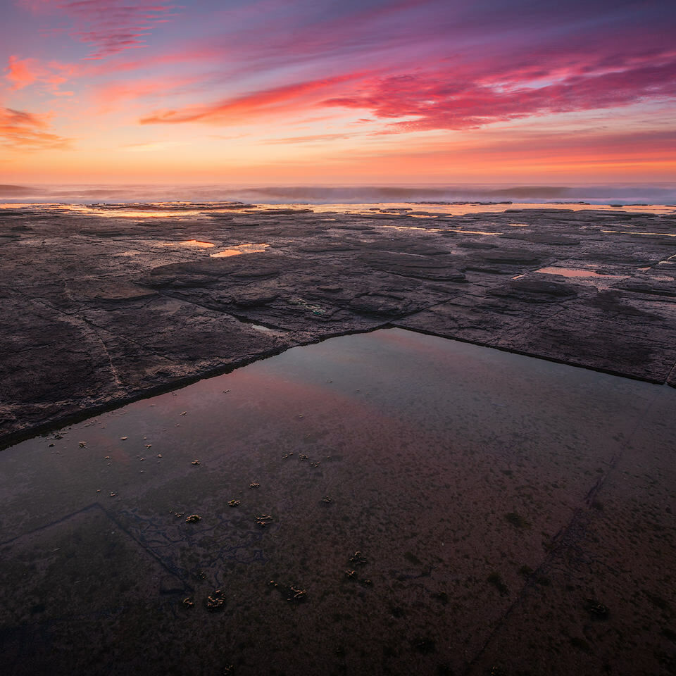 Colourful sunrise over geometric tidepool formations on the coast of South Africa
