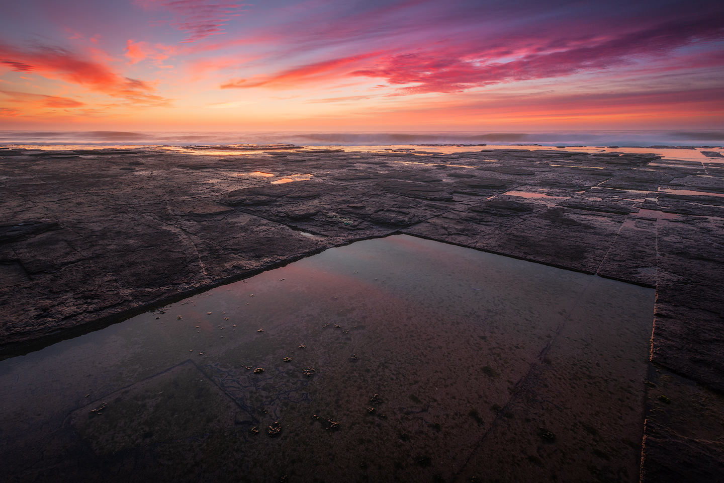 Colourful sunrise over geometric tidepool formations on the coast of South Africa
