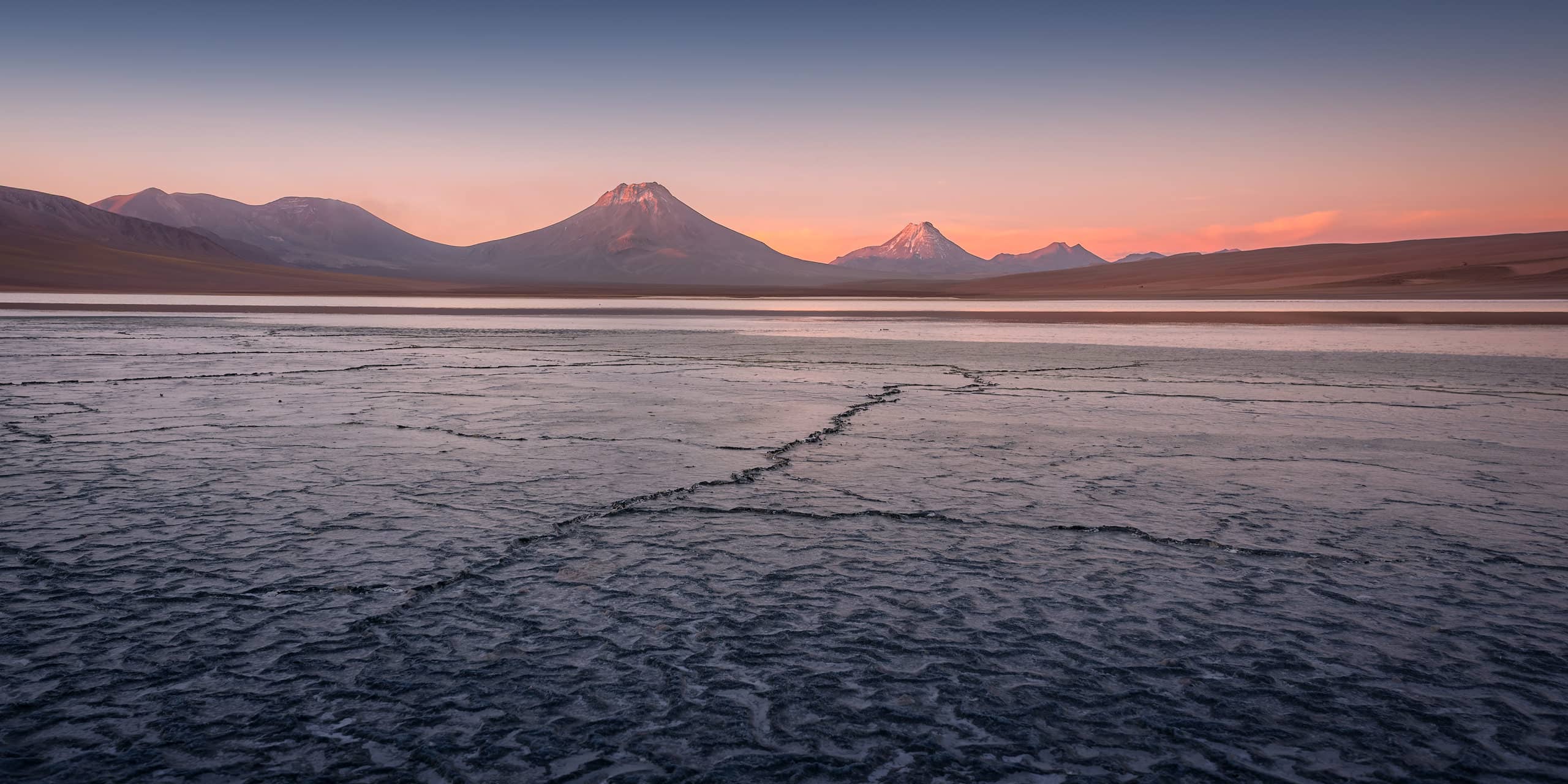 Salt flat in the Andes with volcanic peaks&nbsp;at sunset